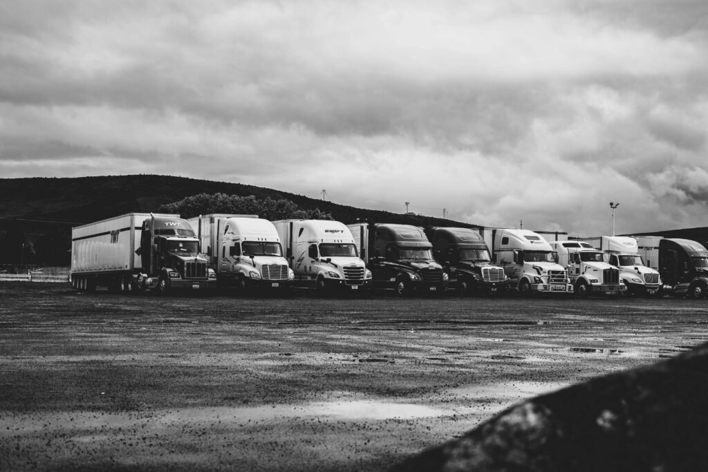 pexels-photo-2348359-2348359 Row of parked semi trucks in a rainy lot, captured in a dramatic black and white setting.